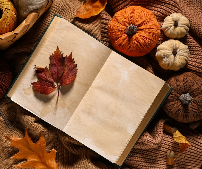 Open journal with a red autumn leaf, surrounded by pumpkins, knit blankets, and fall foliage.